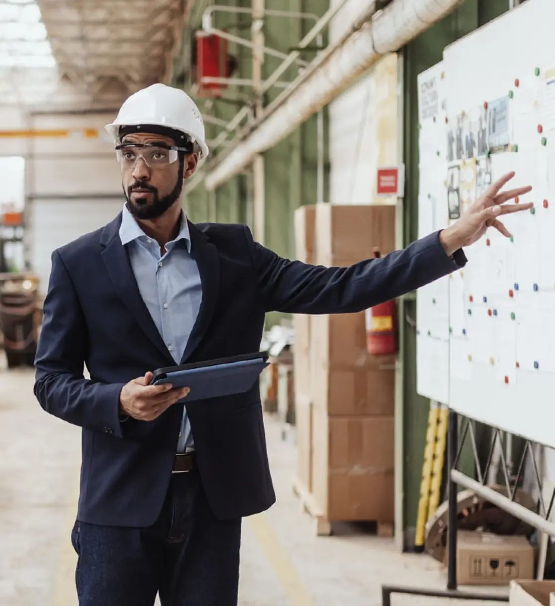 Factory owner explaining plans to improve efficiency to his employees in front of a Kanban board. 
