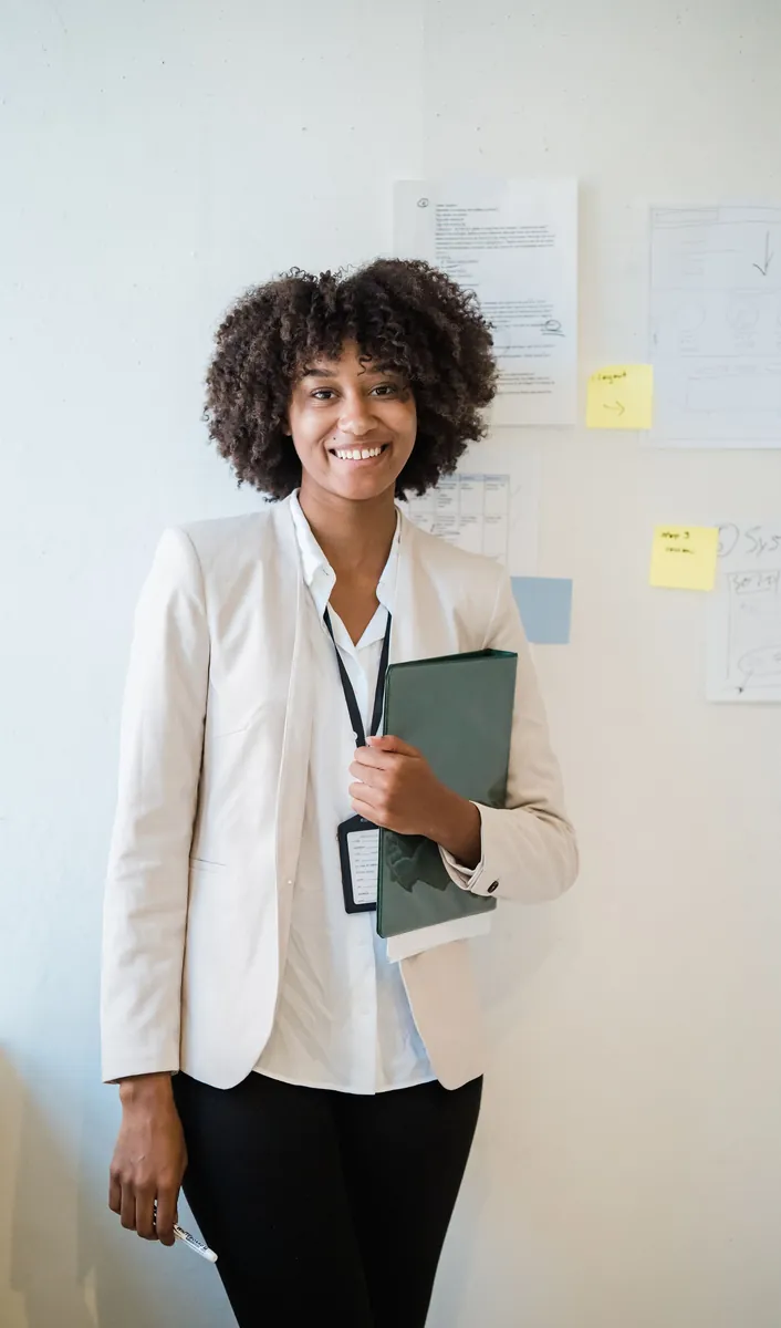 Smiling professional woman in a white blazer holding a folder in a bright office