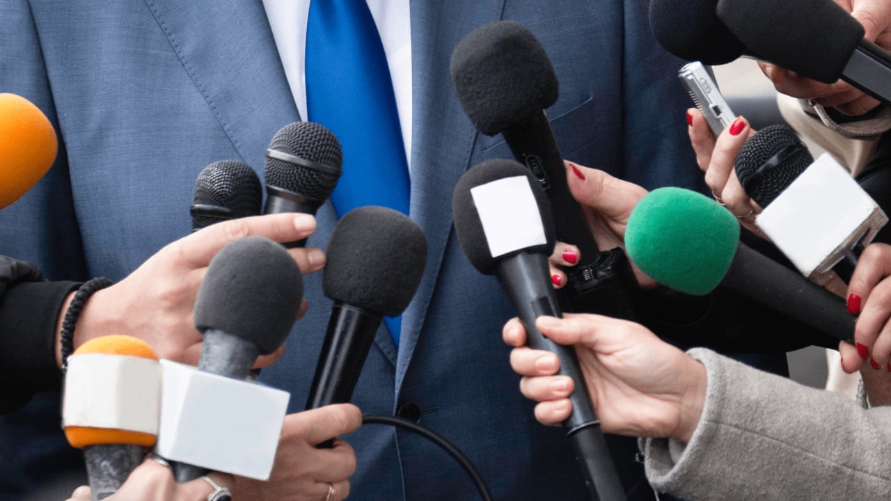 Un homme en costume entouré de micros et de nombreux journalistes