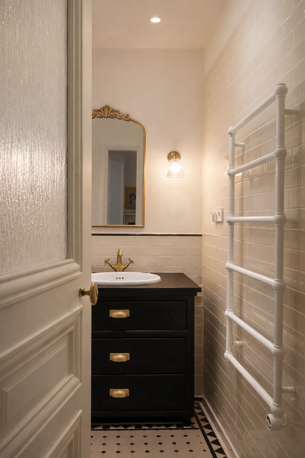 Salle de bains rénovée avec meuble vasque sombre, robinetterie en laiton et carrelage noir et blanc