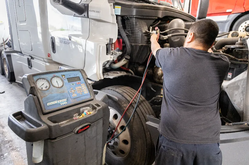 Technician servicing truck HVAC system using a CoolTech 34788 machine with hood open and gauges connected.