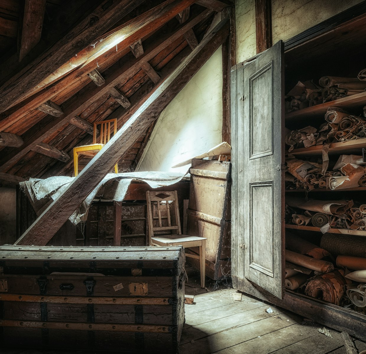 Grenier encombré d'une malle ancienne, de chaises et de rouleaux, avant un débarras
