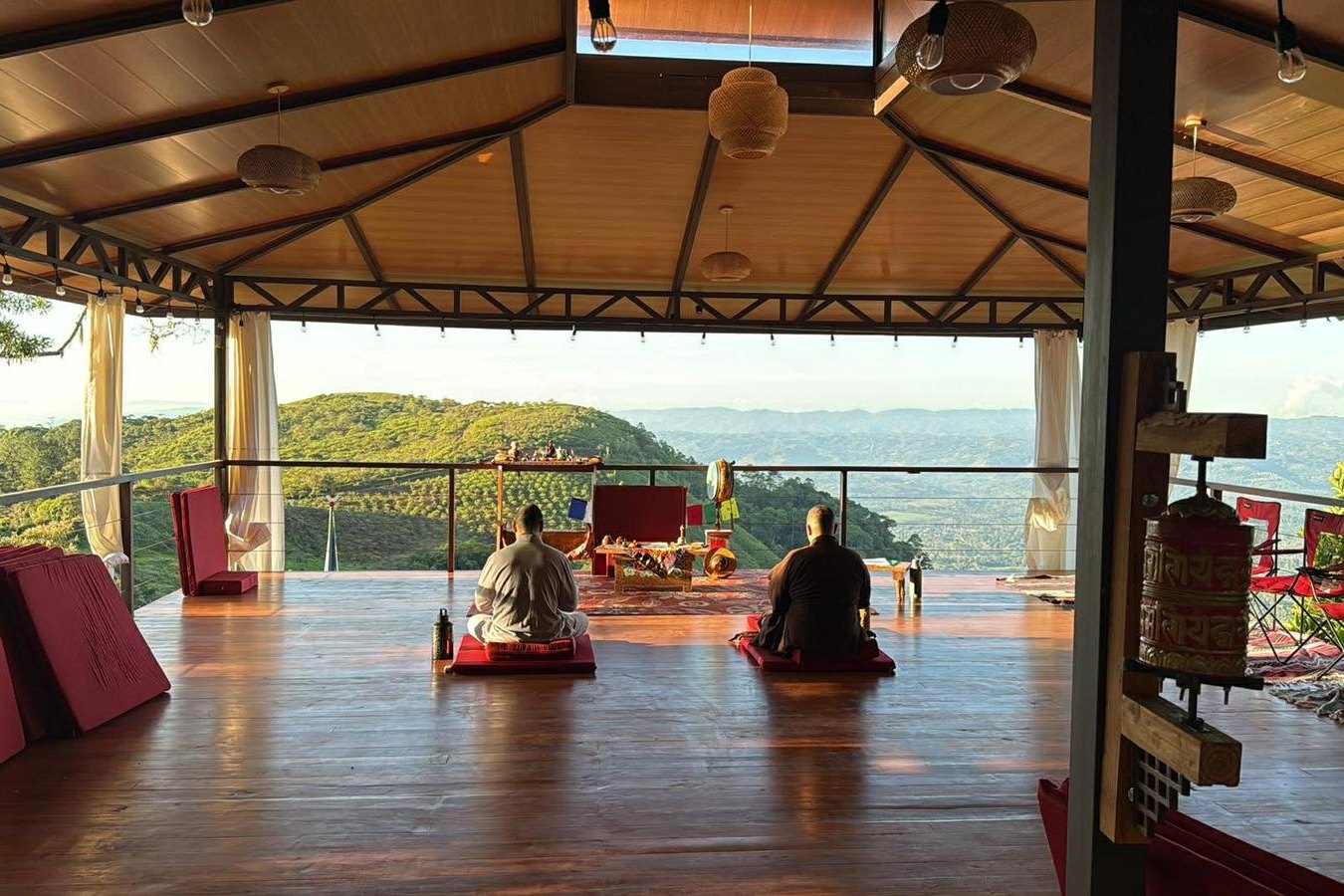 Two people meditating in the open-air meditation hall at Dewachen in the late afternoon light