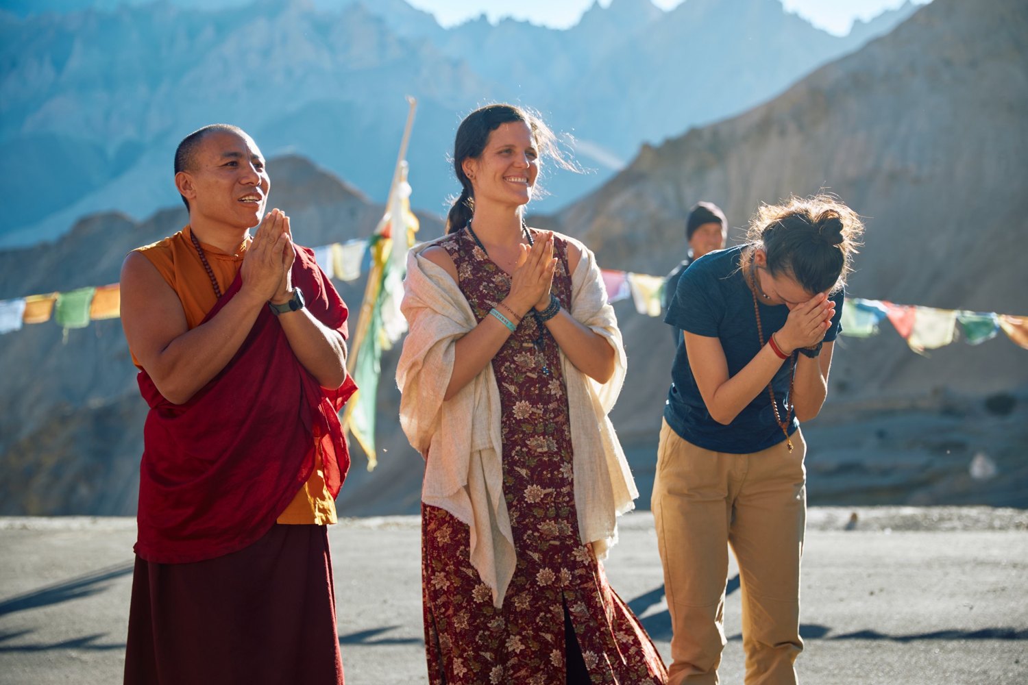 Lama Dorje and two students with hands joined under prayer flags in the mountains of Nepal