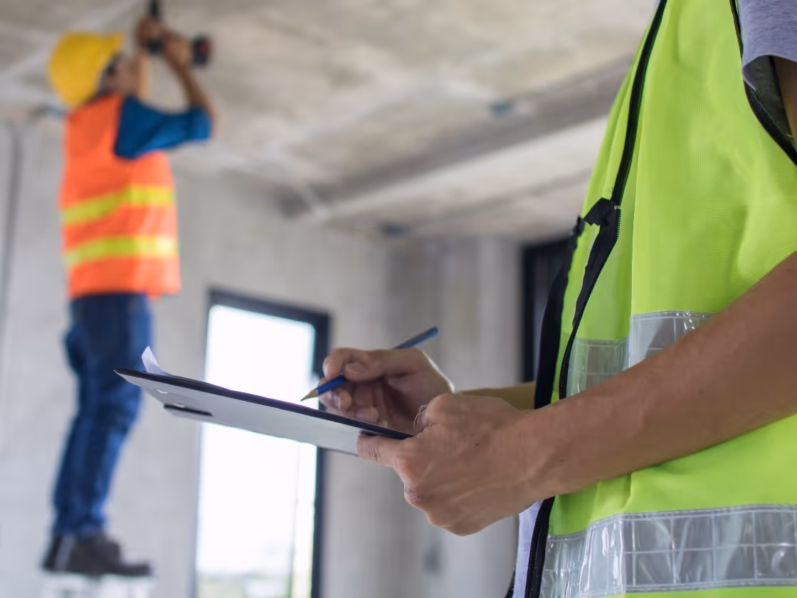 Construction workers in safety vests reviewing plans on clipboard at site