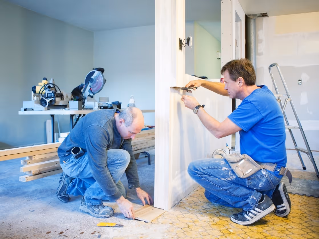 Two workers installing flooring and wall materials in home renovation project