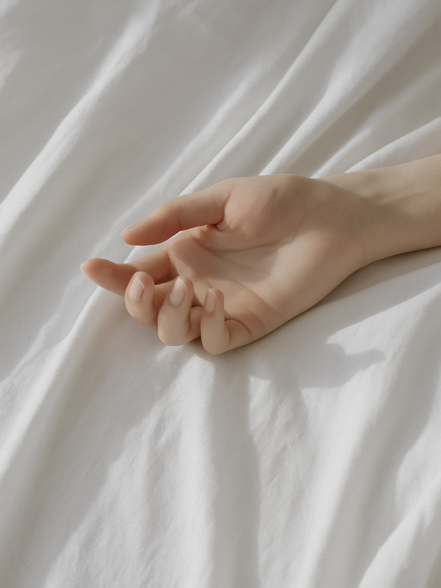 A womans hand resting on a white bed sheet