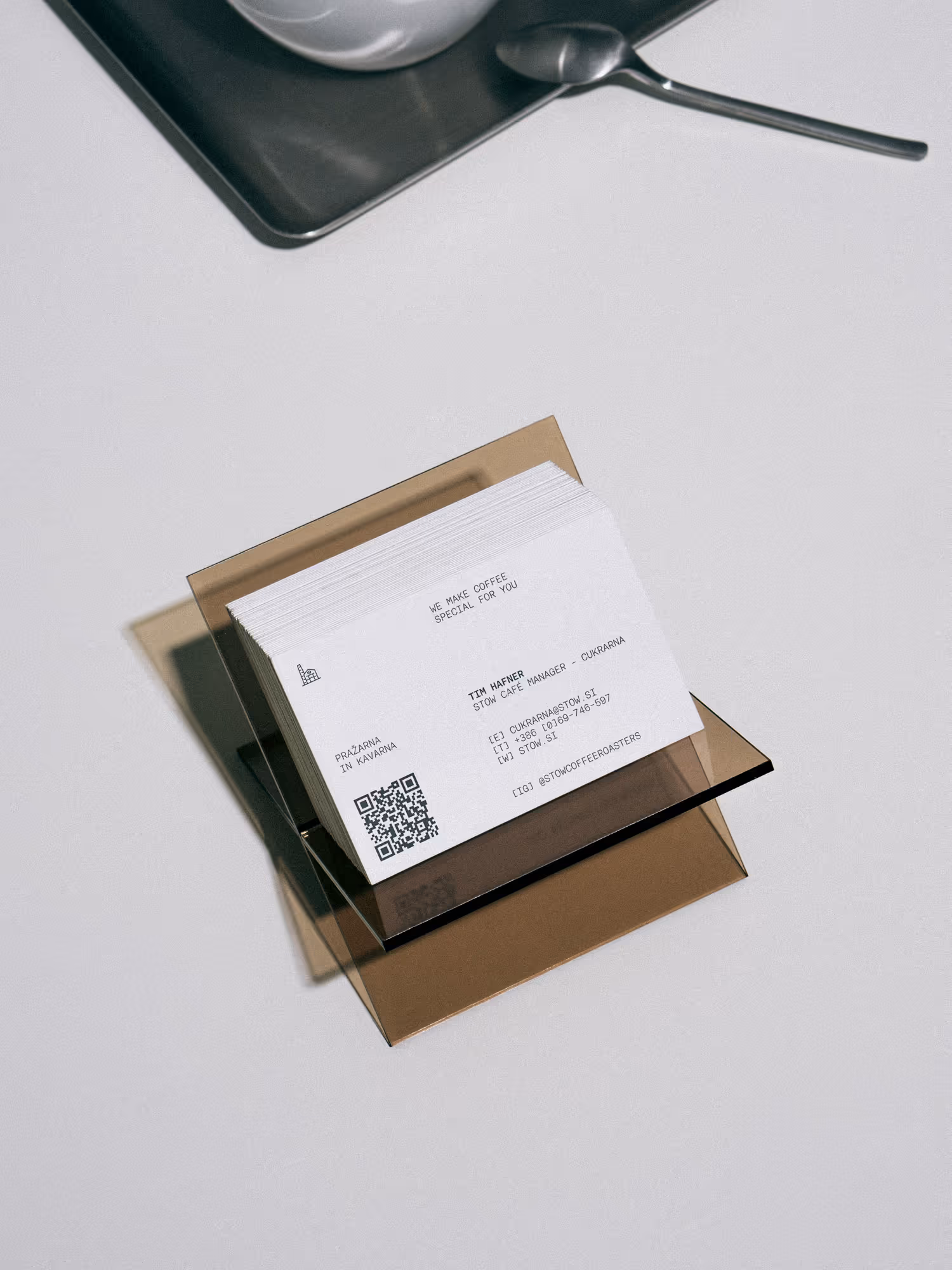 Stack of business cards for Tim Hafner, Stow Caffe Manager, placed in a transparent brown holder on a white surface with a metal tray and spoon partially visible.