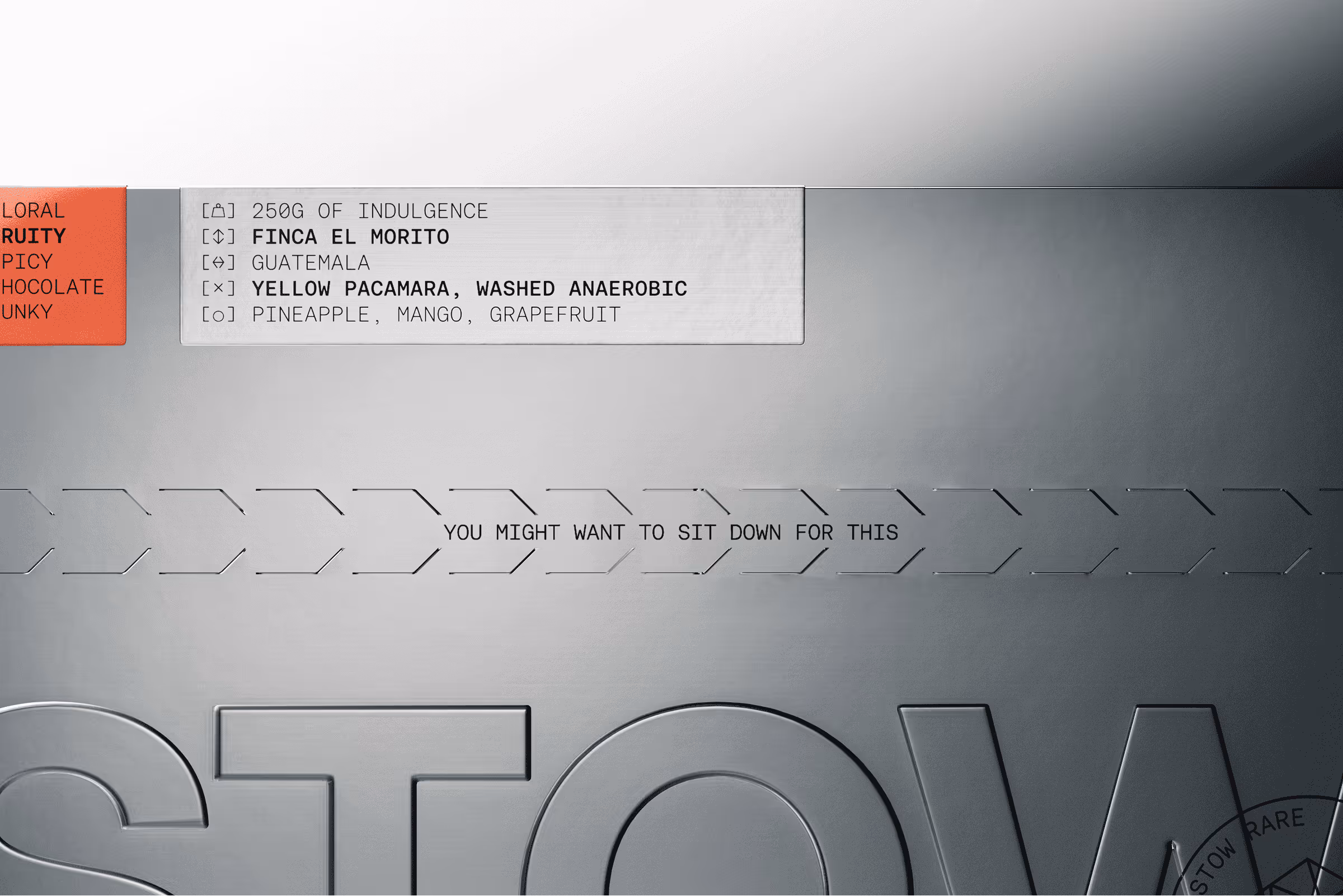 Metallic surface with embossed text 'STOW' and labels indicating coffee details including '250G of Indulgence', 'Finca El Morito', 'Guatemala', 'Yellow Pacamara, Washed Anaerobic', and flavor notes 'Pineapple, Mango, Grapefruit'.