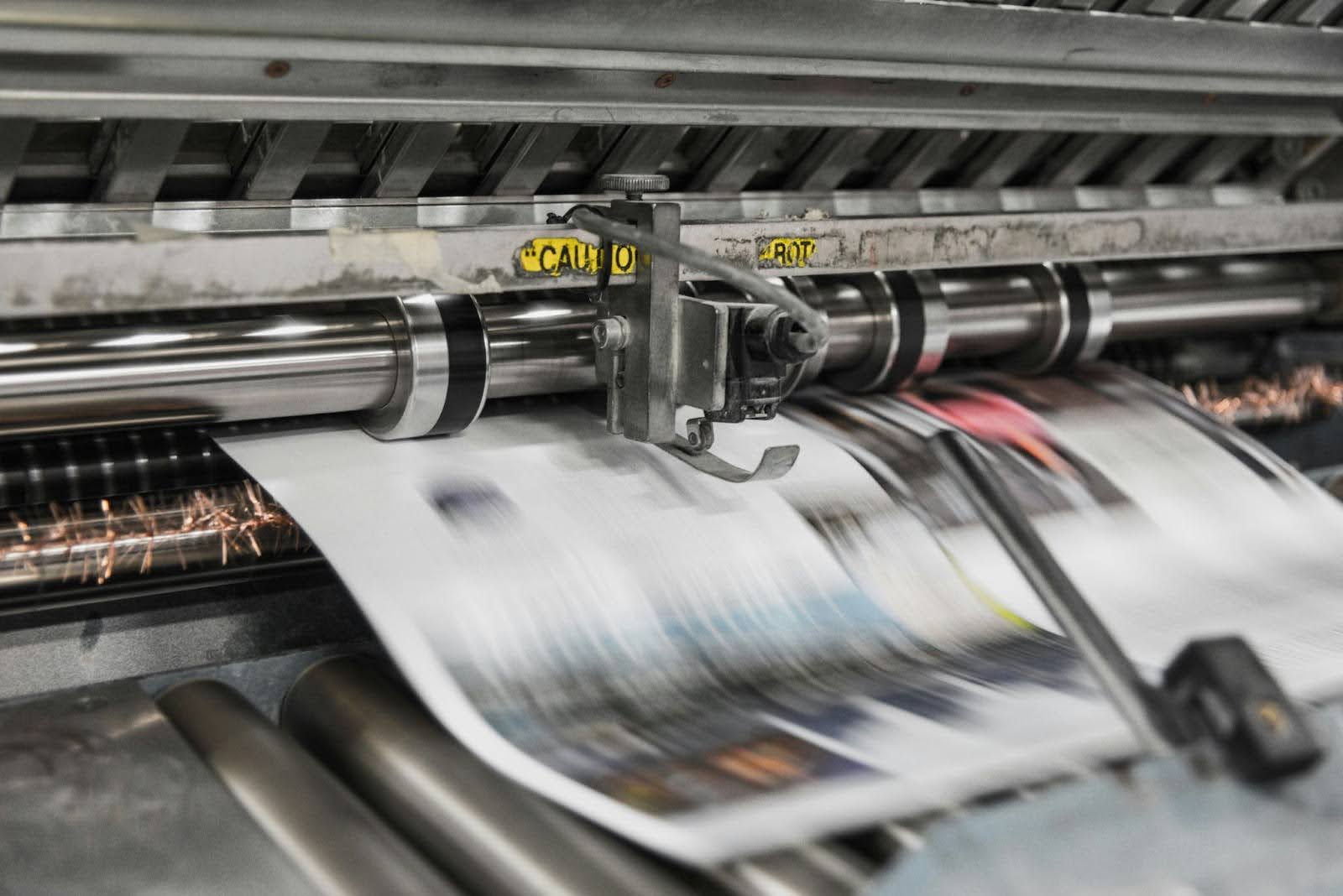A close-up shot of a high-speed industrial printing press, with blurred sheets of paper moving rapidly through metal rollers.