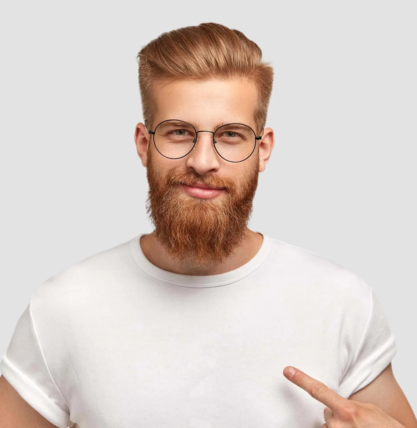 Bearded man with glasses and styled hair smiling while pointing to his white t-shirt.