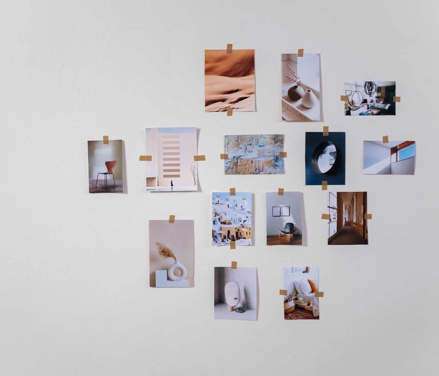 A white wall with fifteen small photos and art prints taped in a loose grid, featuring minimalist and architectural themes, a chair, vases, and abstract scenes.