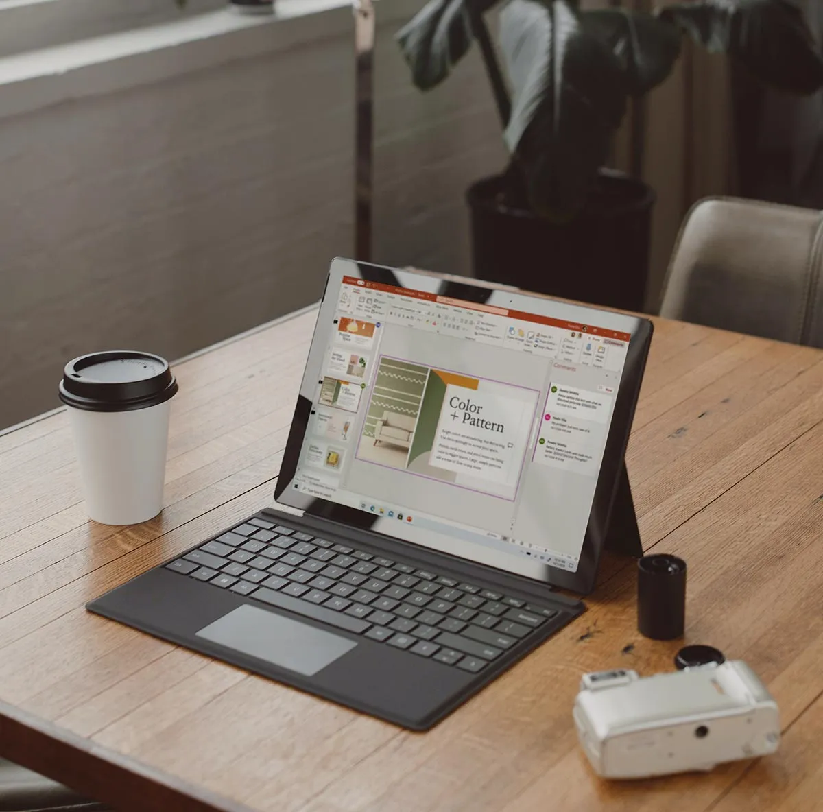 Tablet with keyboard showing a presentation slide titled 'Color + Pattern' on a wooden table next to a white disposable coffee cup and a white camera with a film roll.