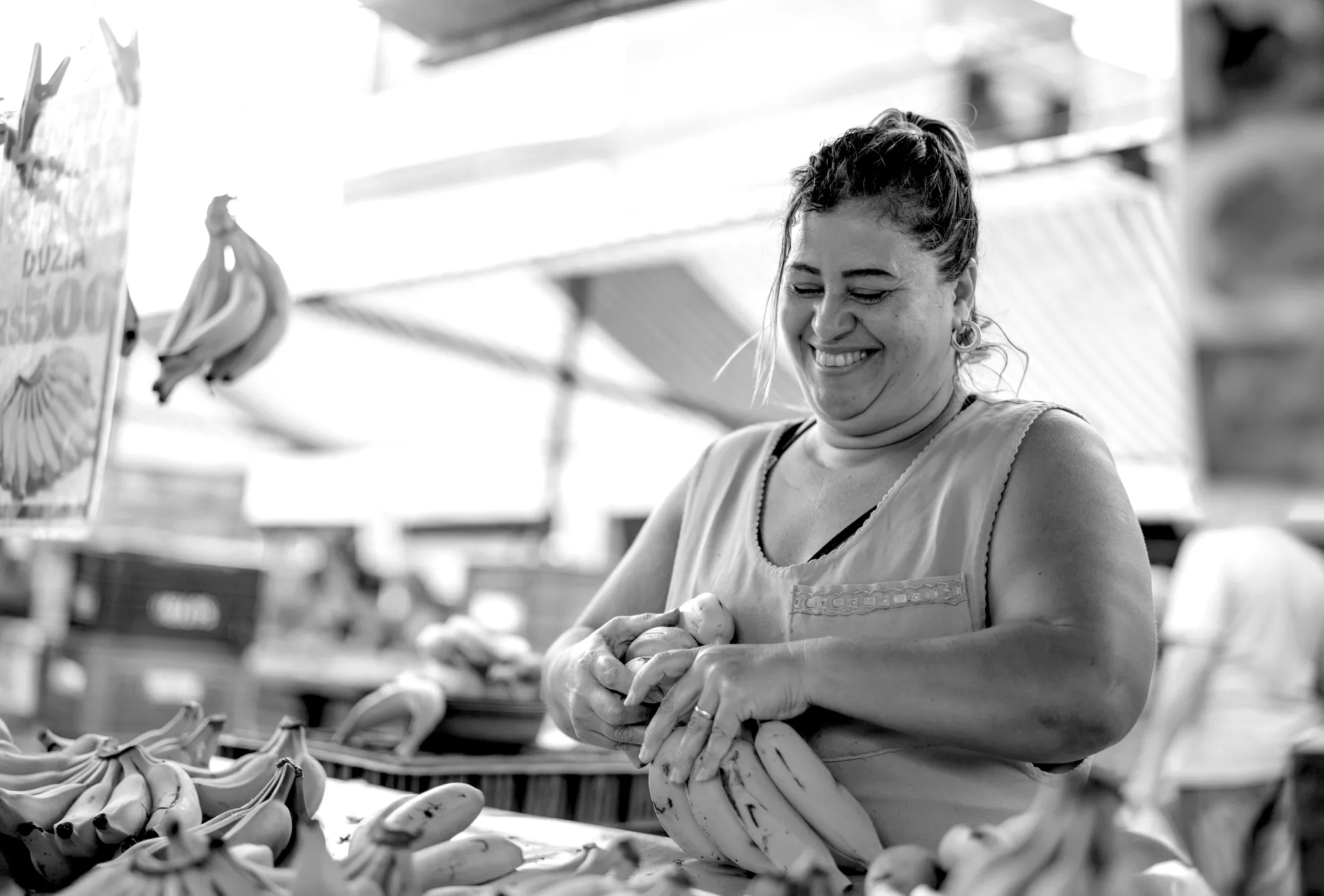 Smiling woman arranging bunches of bananas at a market stall.