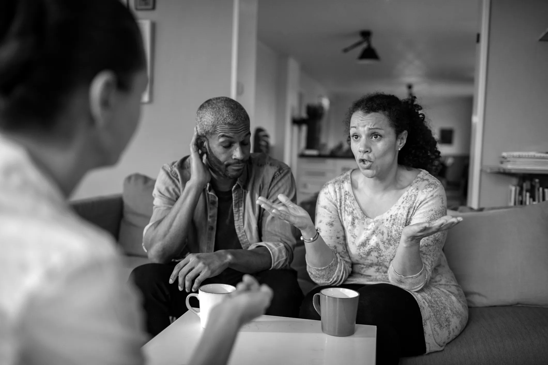 Couple having a serious conversation with a third person in a living room, woman speaking passionately and man looking thoughtful.