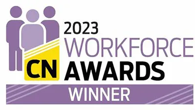 Smiling man with a beard wearing a light blue collared shirt against a plain background.