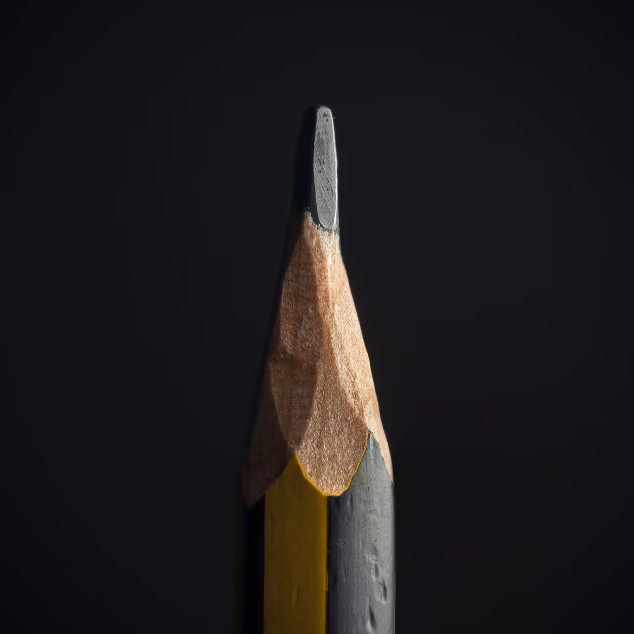 Close-up of the sharpened tip of a yellow and black pencil against a dark background.