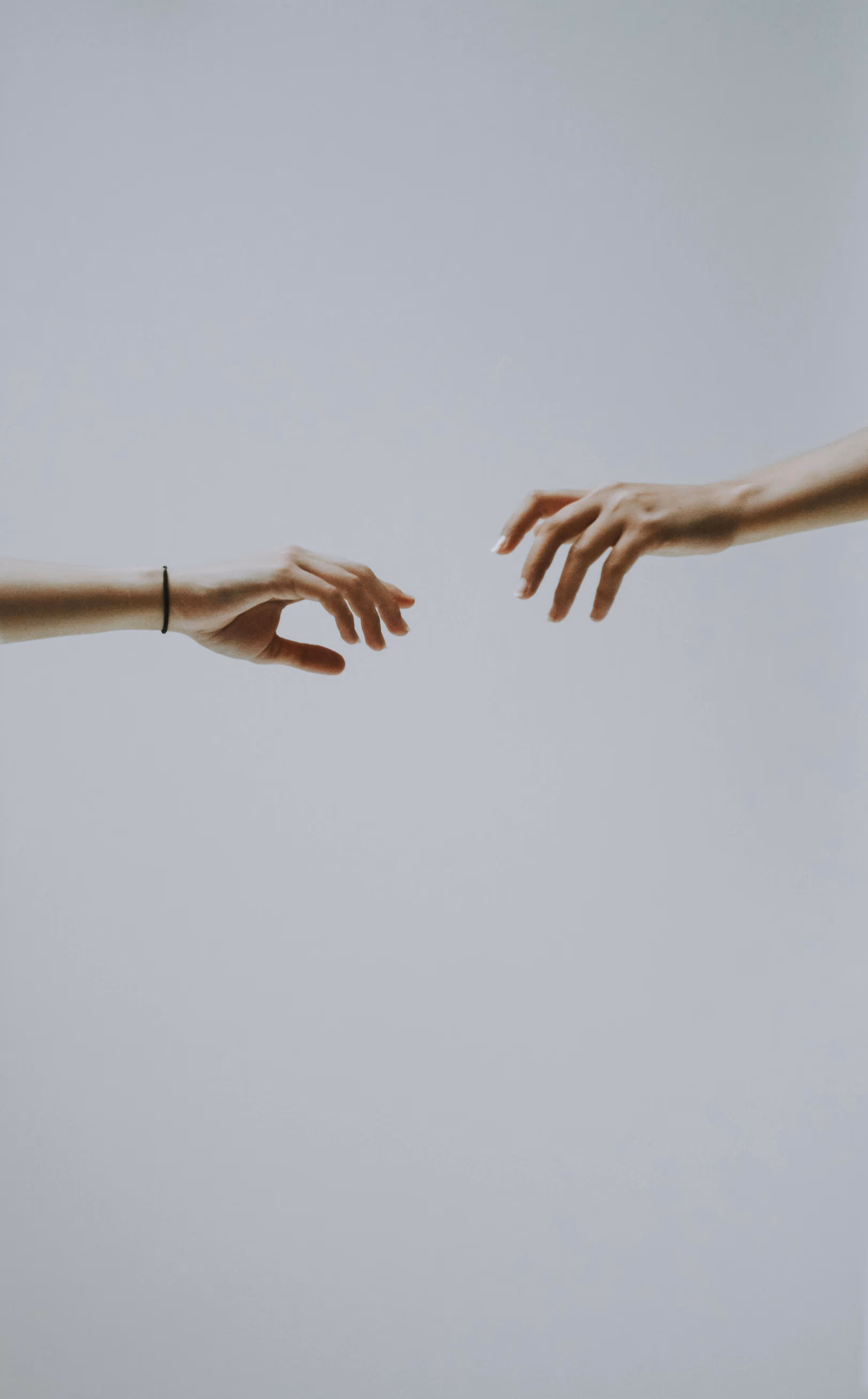 Two outstretched hands reaching towards each other against a plain light gray background.