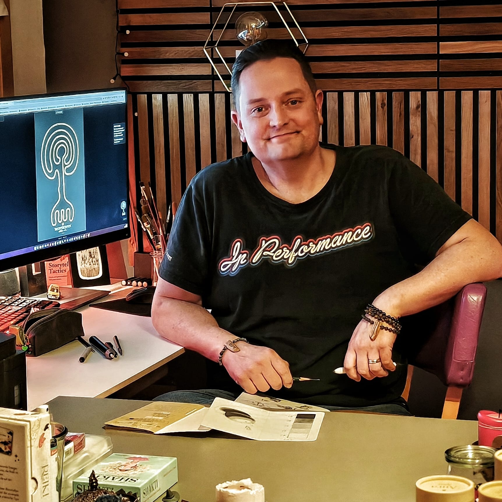 Person in a red hat and white padded vest walking on a rocky mountain trail with snow-capped peaks in the background.