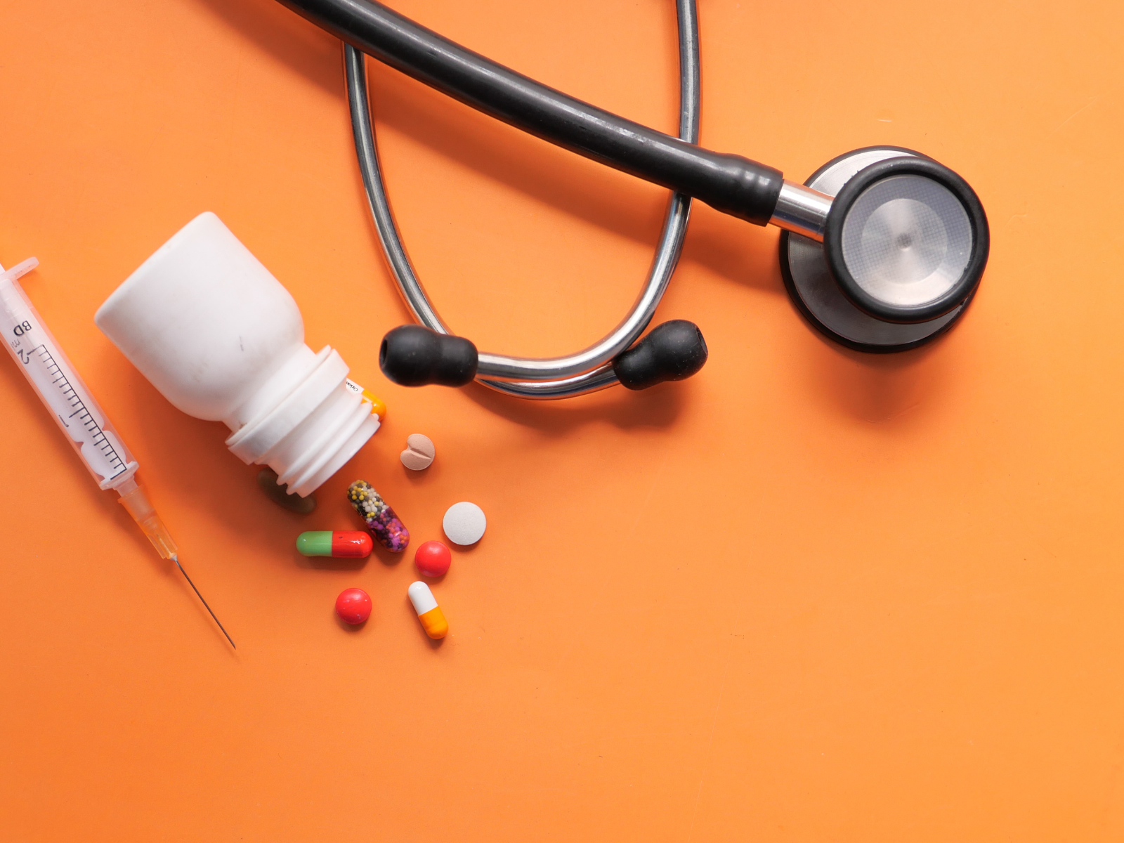 A Syringe, pills, and stethoscope on orange background