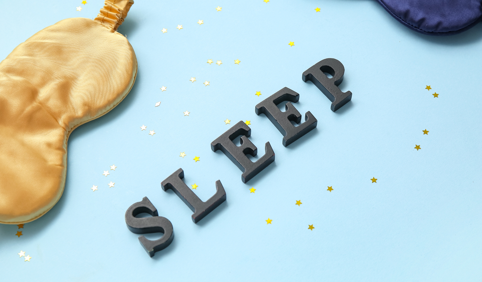 Gold sleep mask on a blue background with the word sleep spelled out 