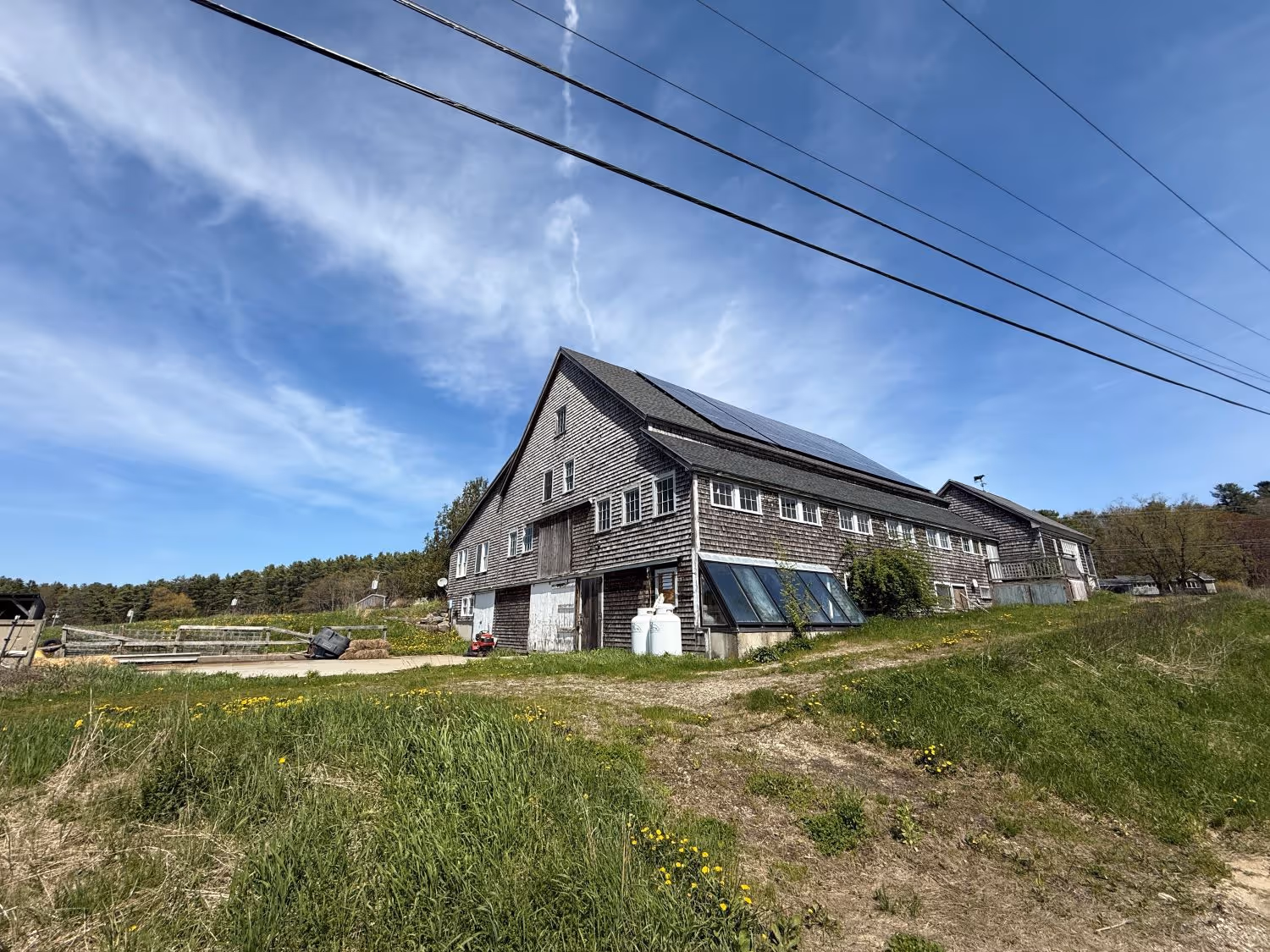 Large wooden building with solar panels on grassy rural property