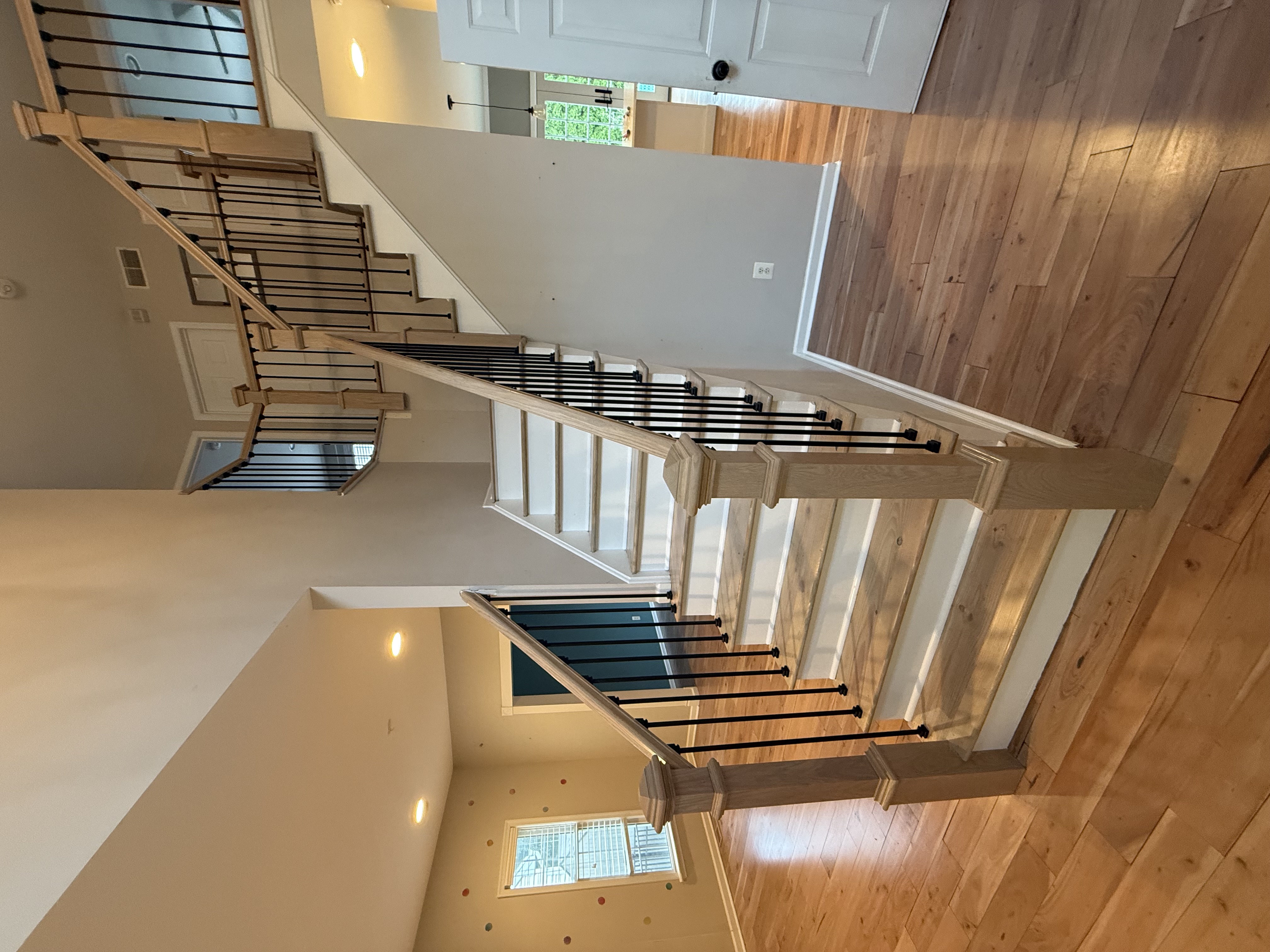 Wooden staircase with light wood steps and black vertical metal balusters in a home with hardwood floors and neutral-colored walls.