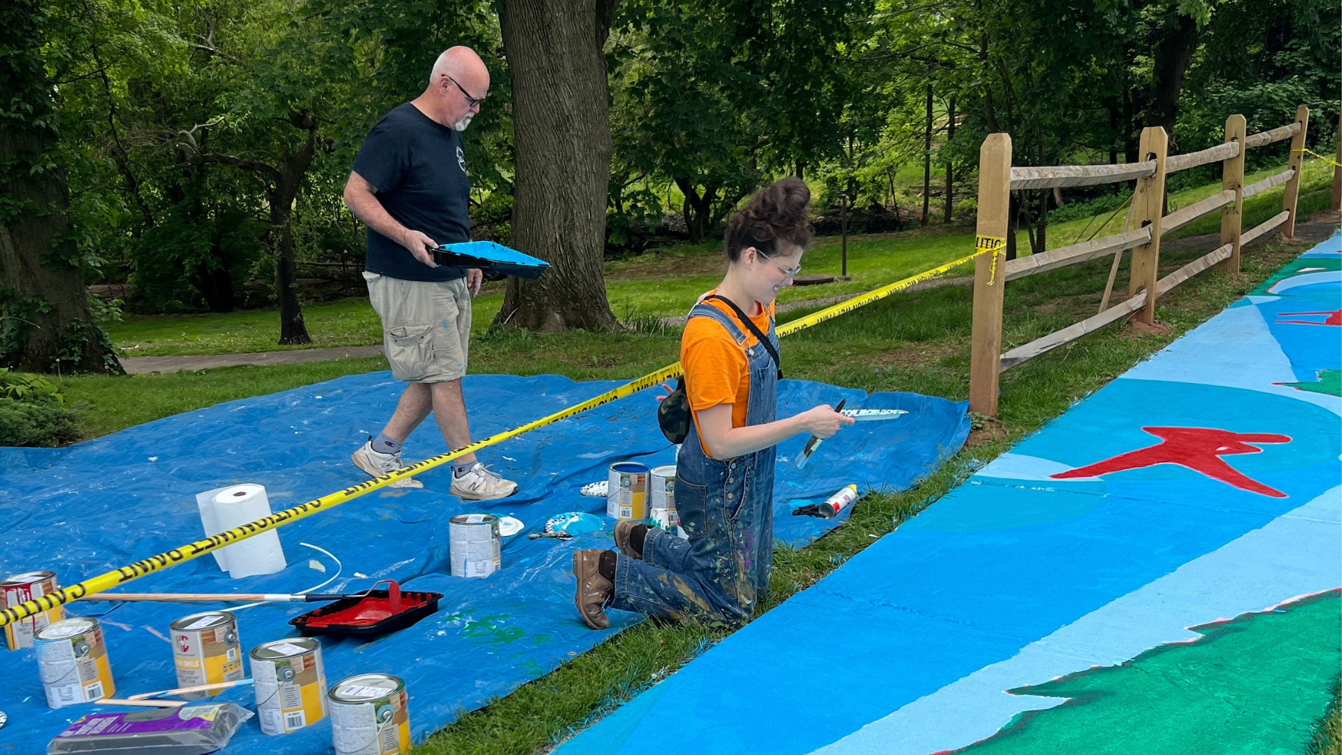 Man in a brown hoodie adjusting framed artwork on a white gallery wall with various paintings.