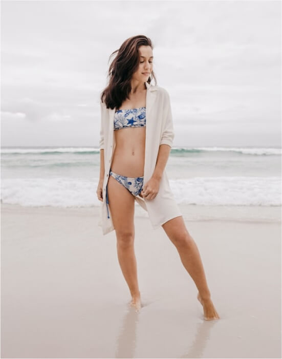 A female model wearing a bikini standing in front of the beach looking away on the left