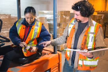 Man teaching safety standards for driving a forklift to an employee