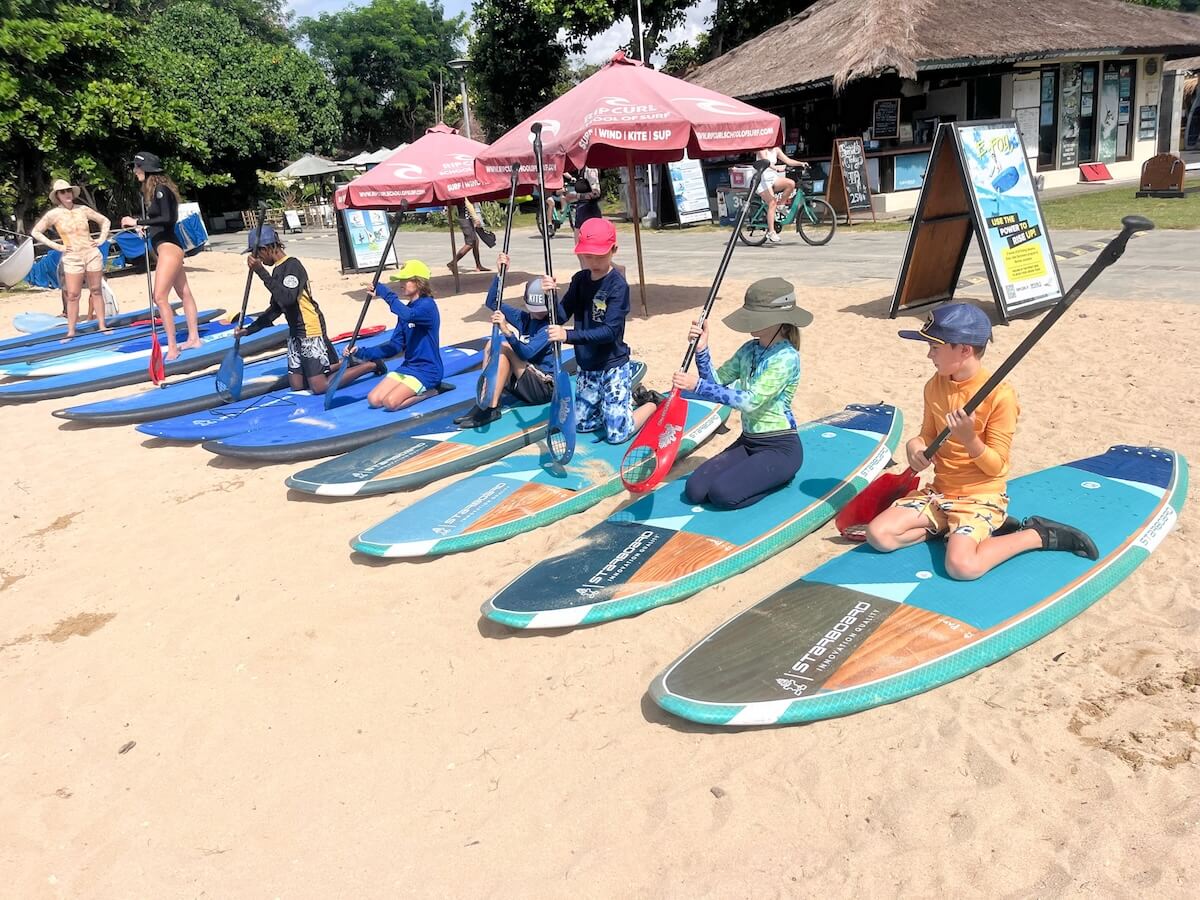 Kids from Boundless Life in Sanur, Bali in collaboration with Rip Curl Surf School practice on paddle boards on the beach.