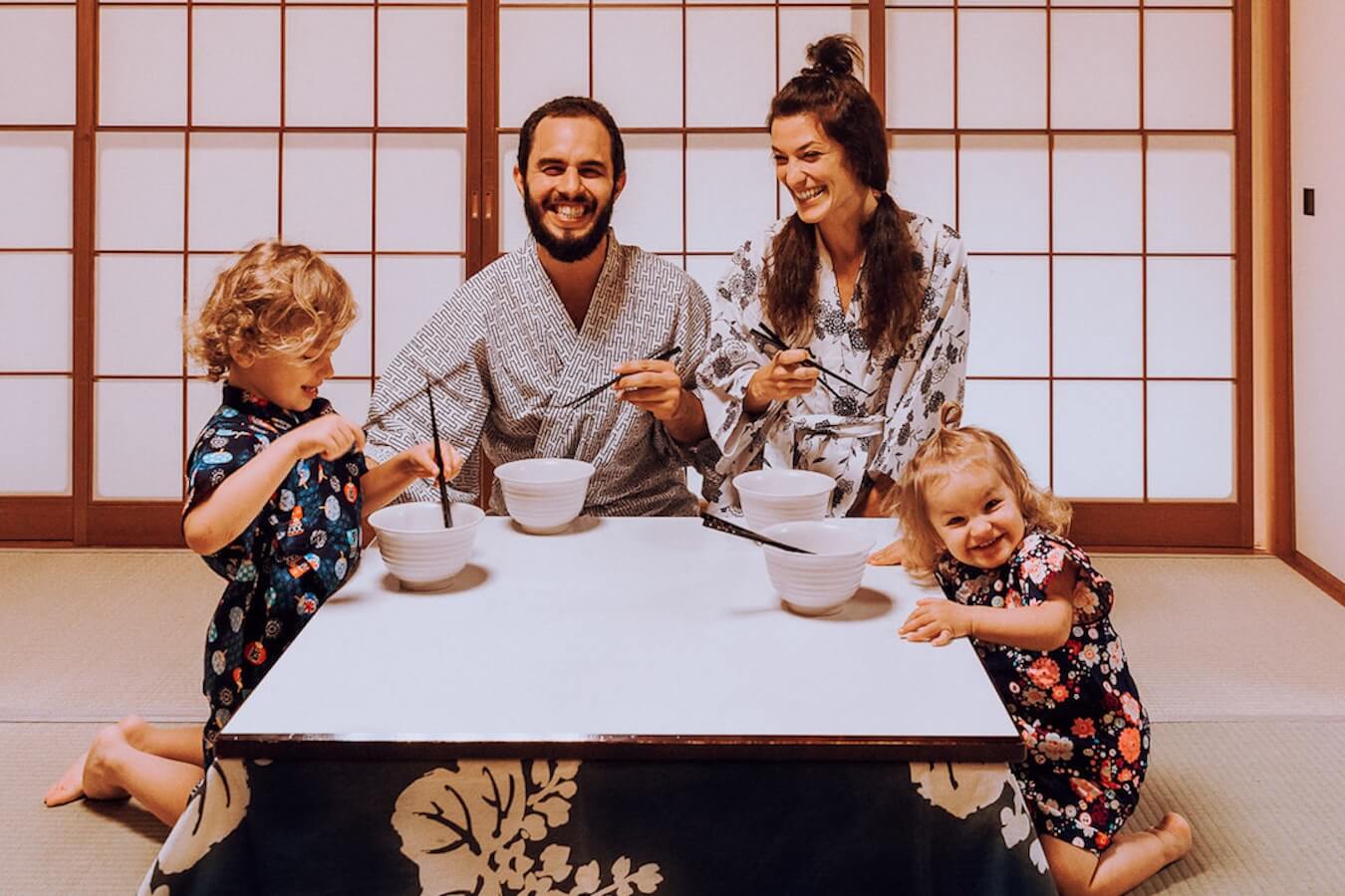 A travel family with two young children sit together laughing for a Japanese meal