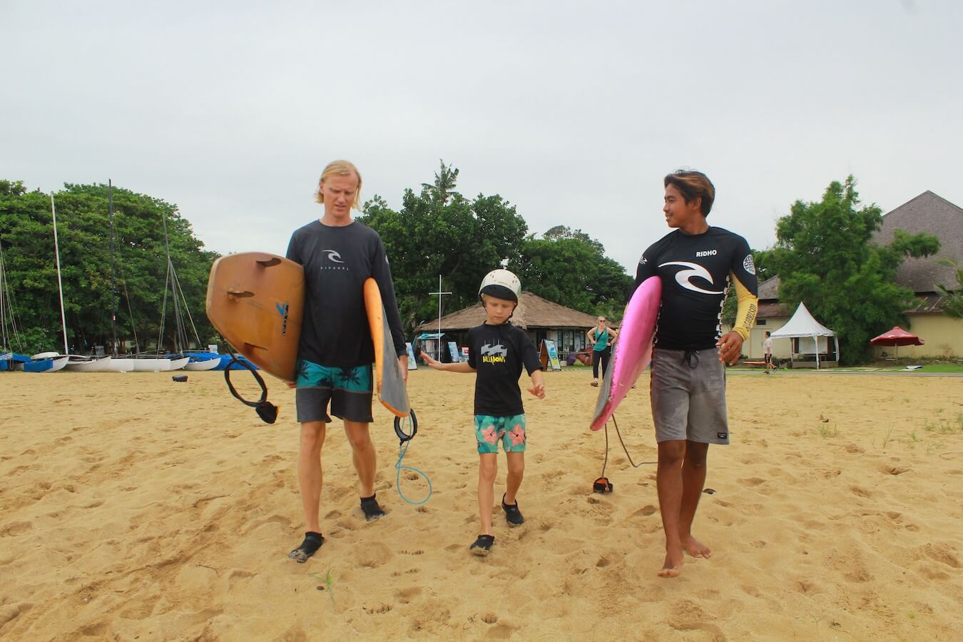 A family walk with their surfboards to the beach in Bali for a lesson.