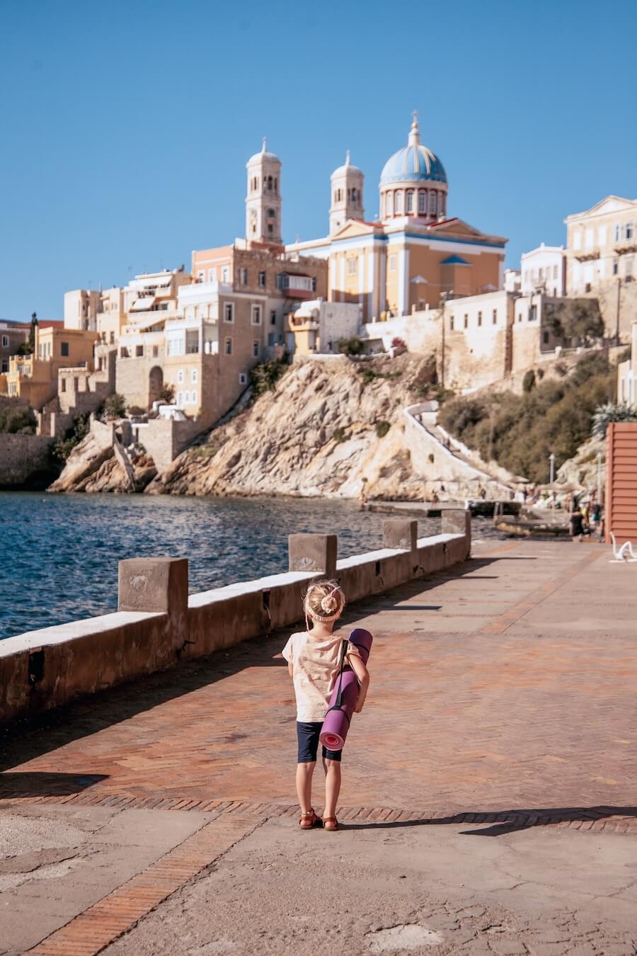 A young child standing with a yoga mat in Syros Greece. 
