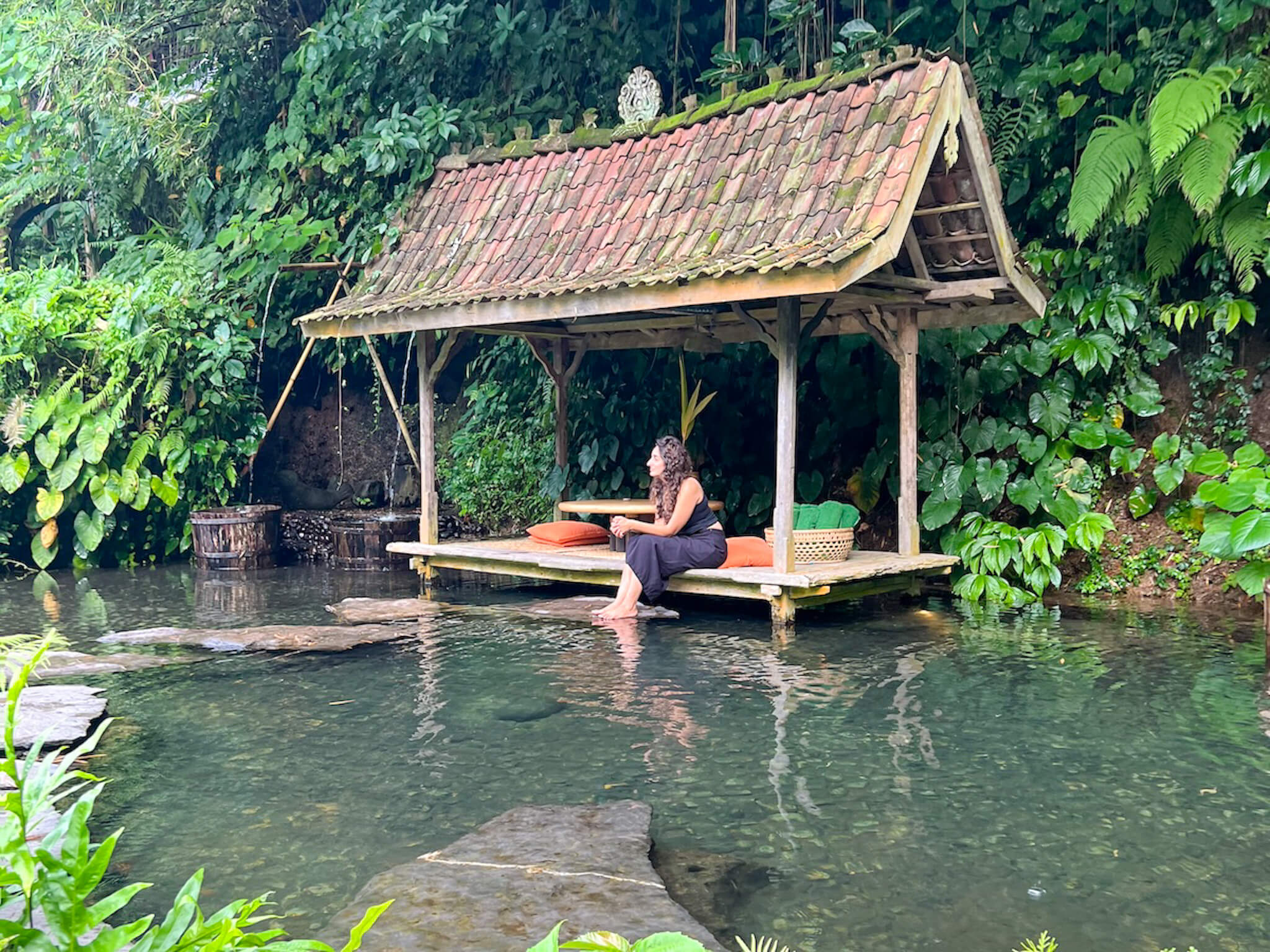 A woman sits in a hut over a river.
