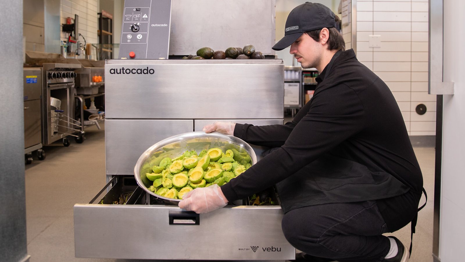 A restaurant worker lifts a bowl of peeled, halved avocados out of the Autocado prep machine