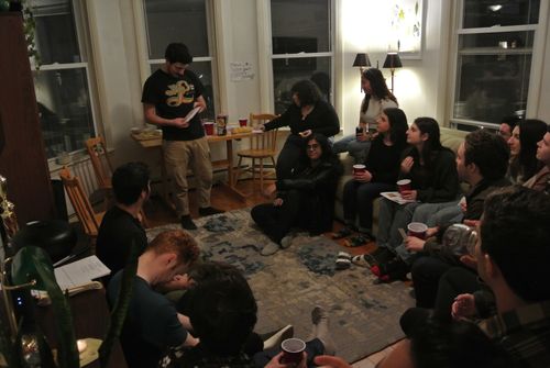 At least 14 members of the break breakers community are sitting around a living room, folks are packed in. Some are on the couch, others on the carpet, many holding drinks, and Matt is about to lead everyone in song. While most are looking at Matt or their source sheets, one member is smiling directly at the camera.