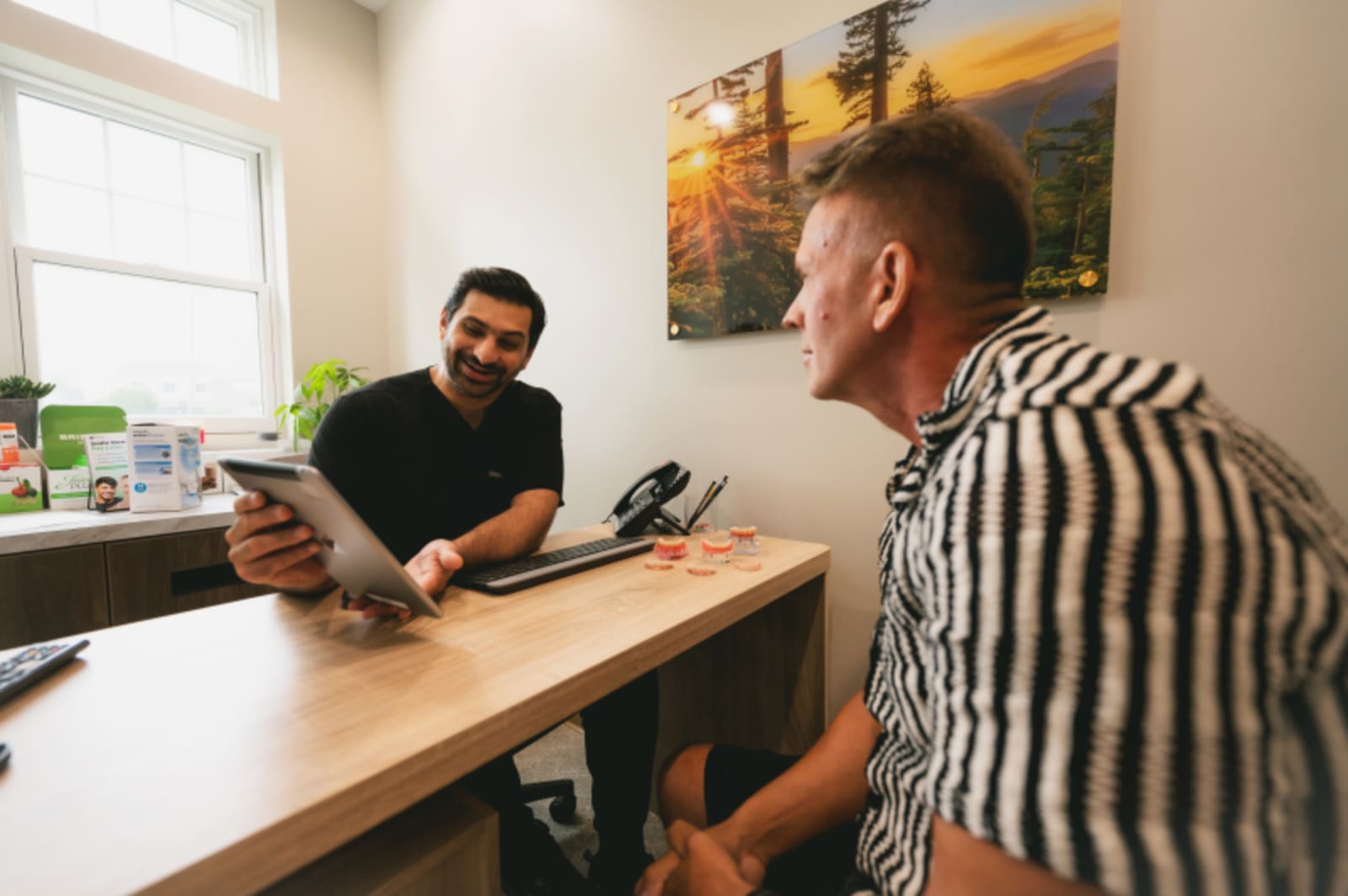 Dentist consulting with male patient at desk in dental office.