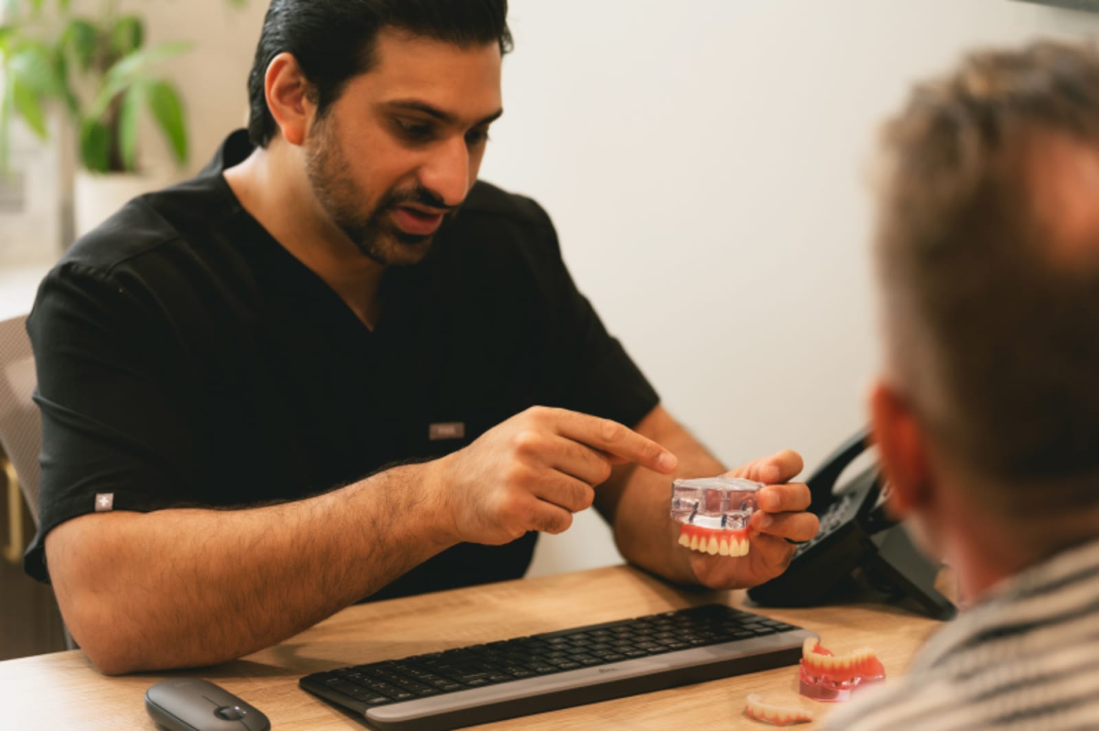 Dentist demonstrating dental implant model to patient during consultation
