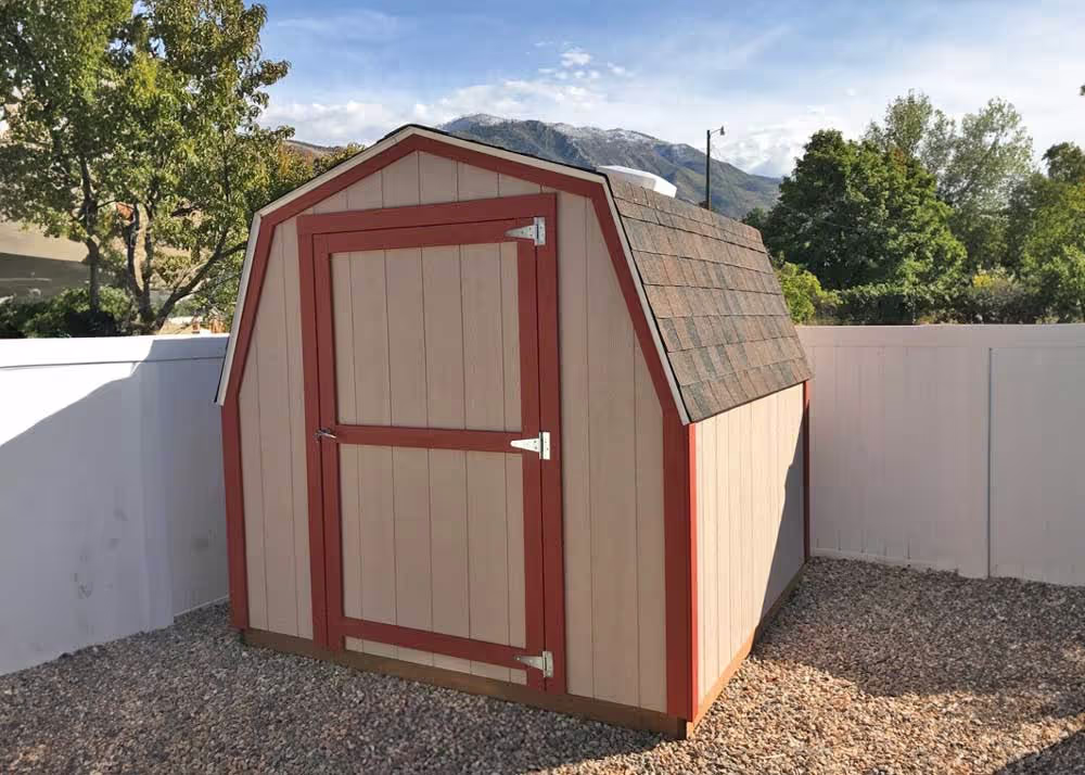An 8 foot by 8 foot mini-barn storage shed in the corner of a backyard