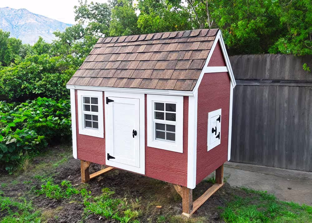 A large hen hut chicken coop with a shingled roof in a back yard