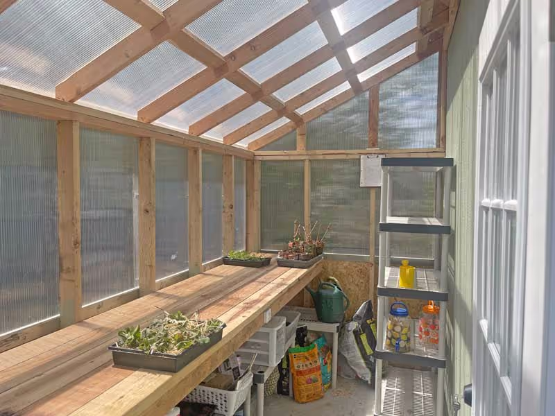 A lean-to greenhouse interior with a redwood workbench used as a potting bench