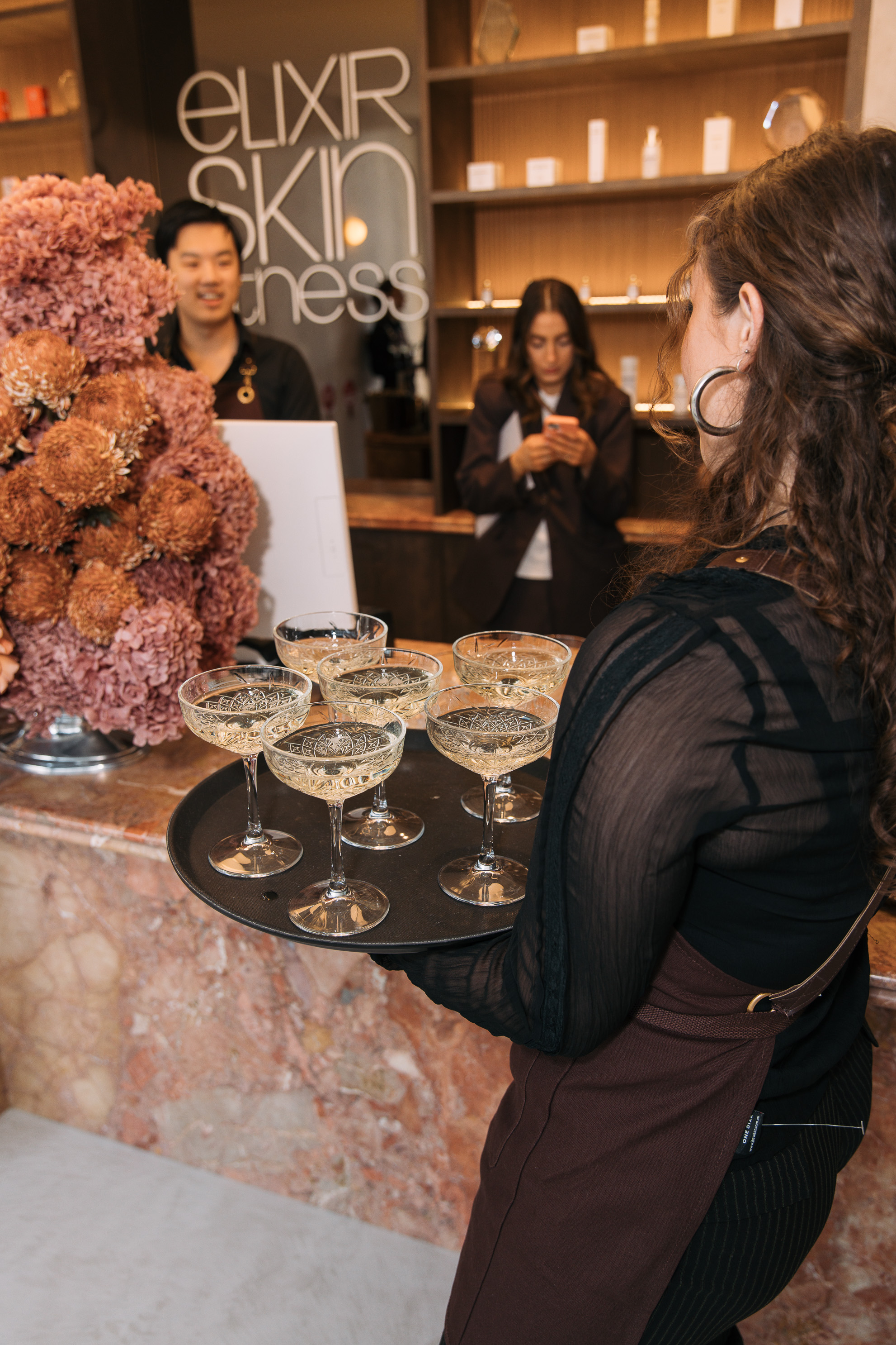 Waitress holding tray with seven filled coupe glasses at the Elixir Launch Event