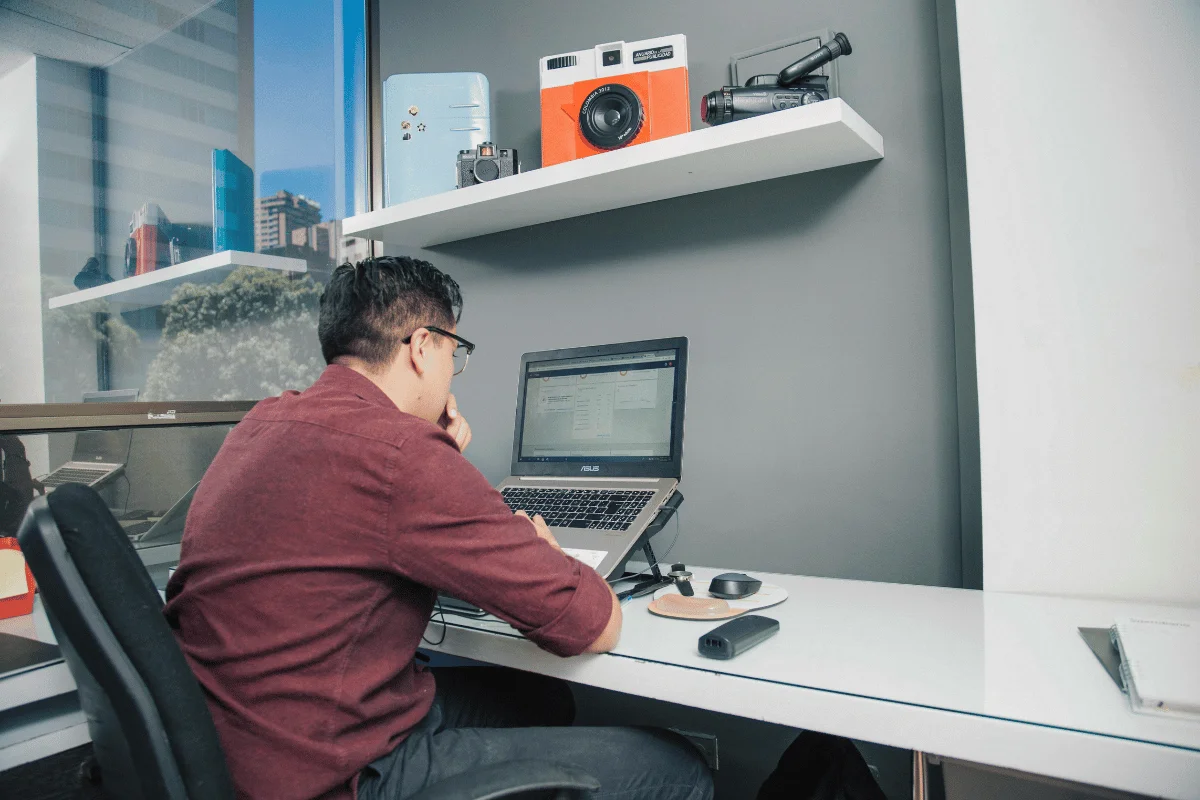Person in a red shirt looking at a laptop screen intently.