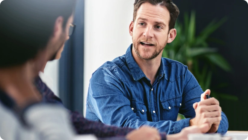 Man in blue denim shirt engaged in conversation with two other people in an indoor setting.