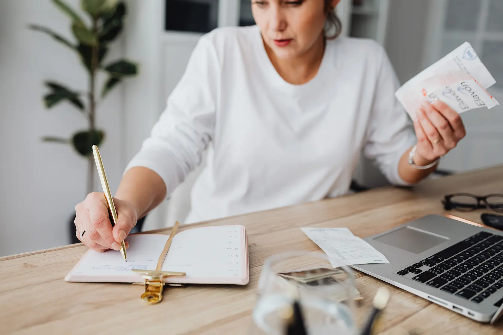 Femme gérant ses finances, écrivant sur un carnet et tenant des reçus à un bureau