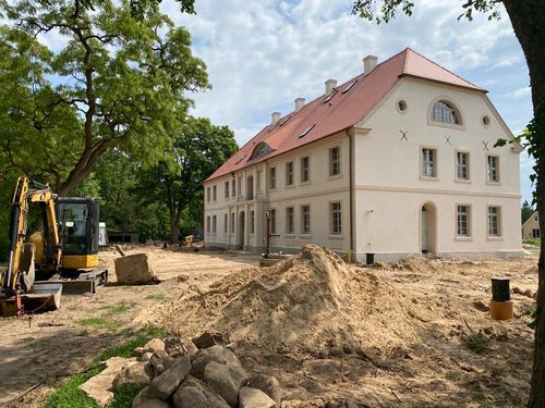 Renoviertes zweistöckiges Gebäude mit Bagger und Bauschutt davor.