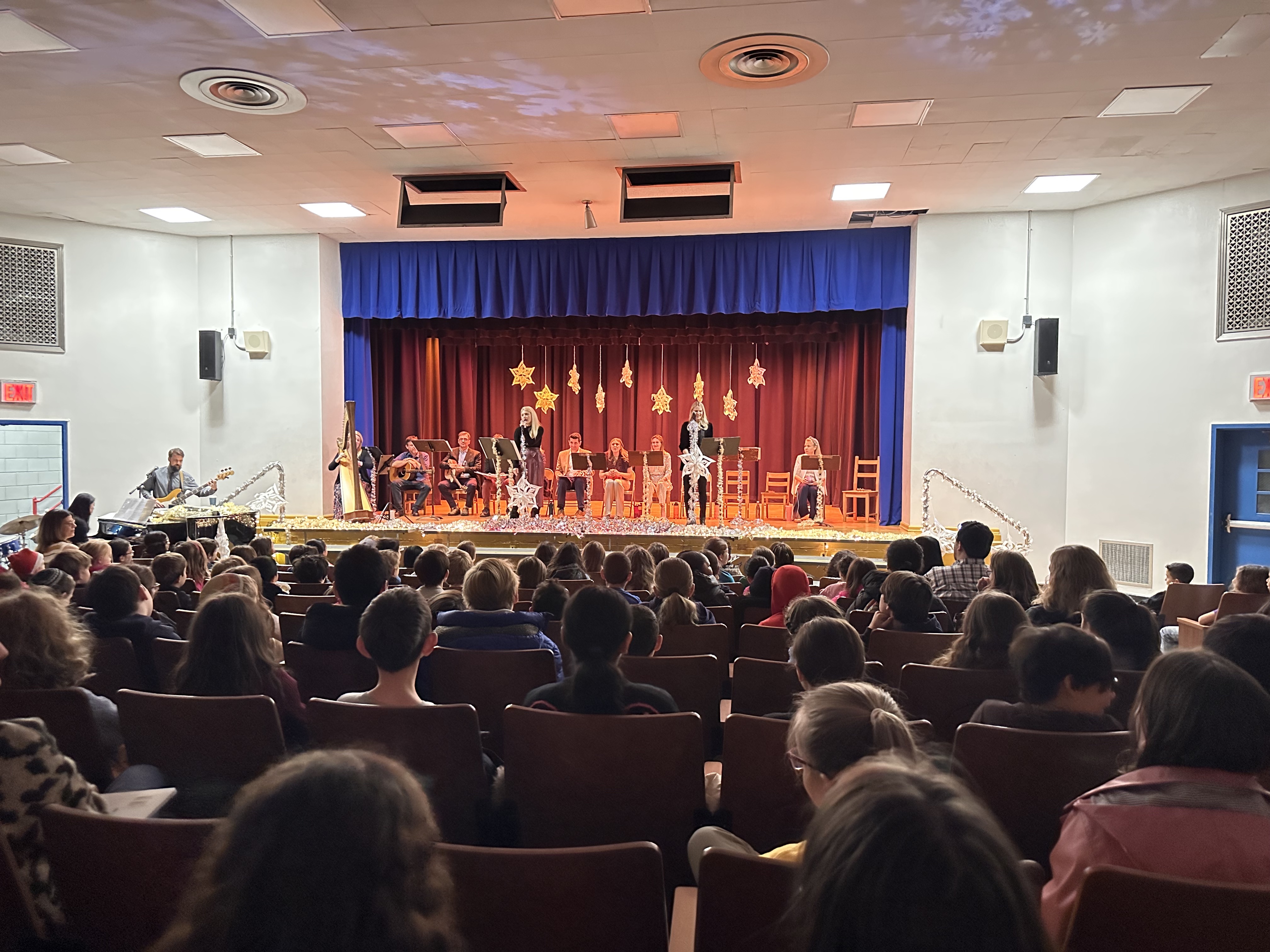 Audience watching a parent music performance with musicians on stage decorated with star-shaped ornaments and festive lights.