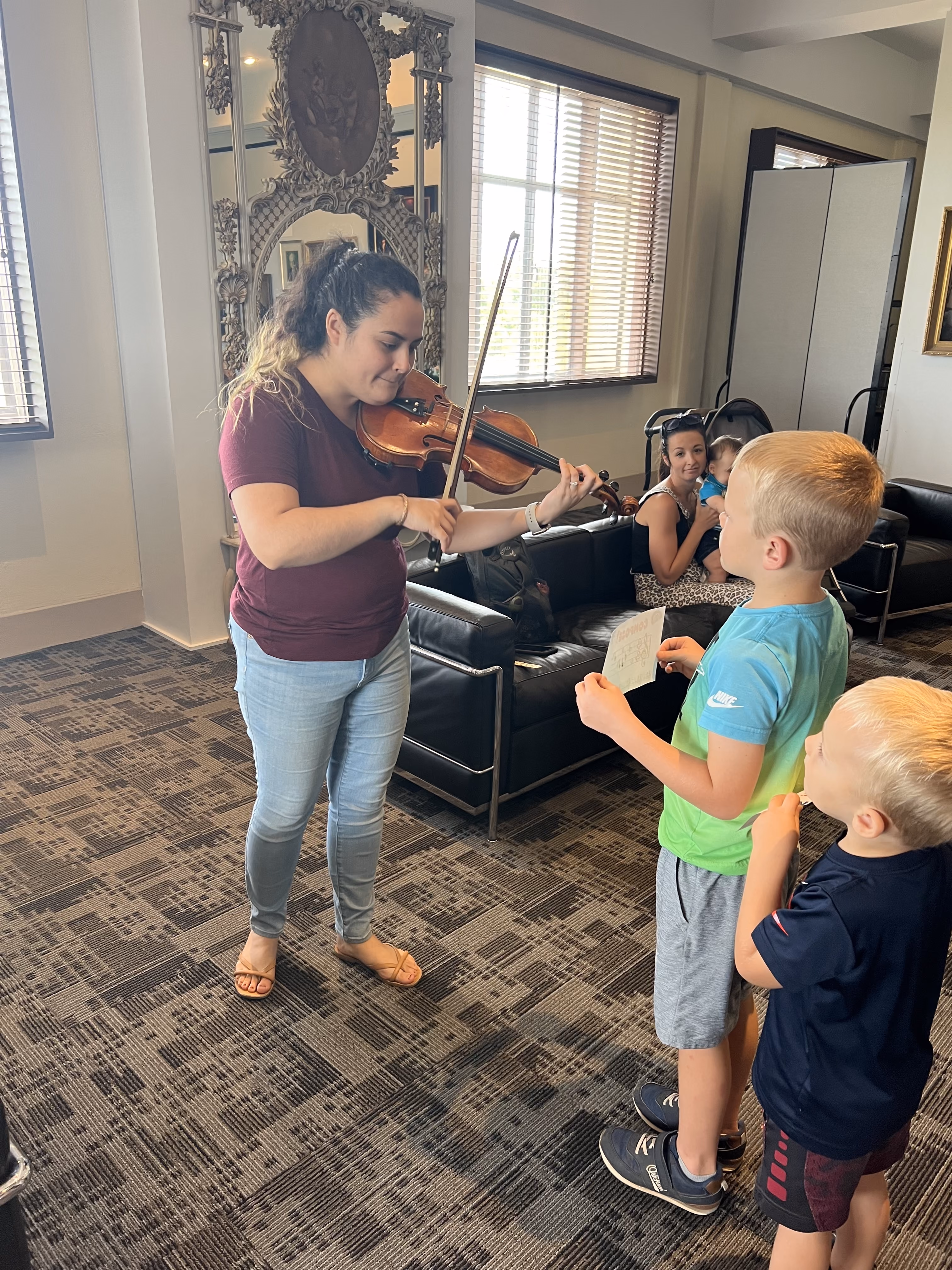 A local female musician plays the violin for a pair of young boys during a music themed Homeschool Day.