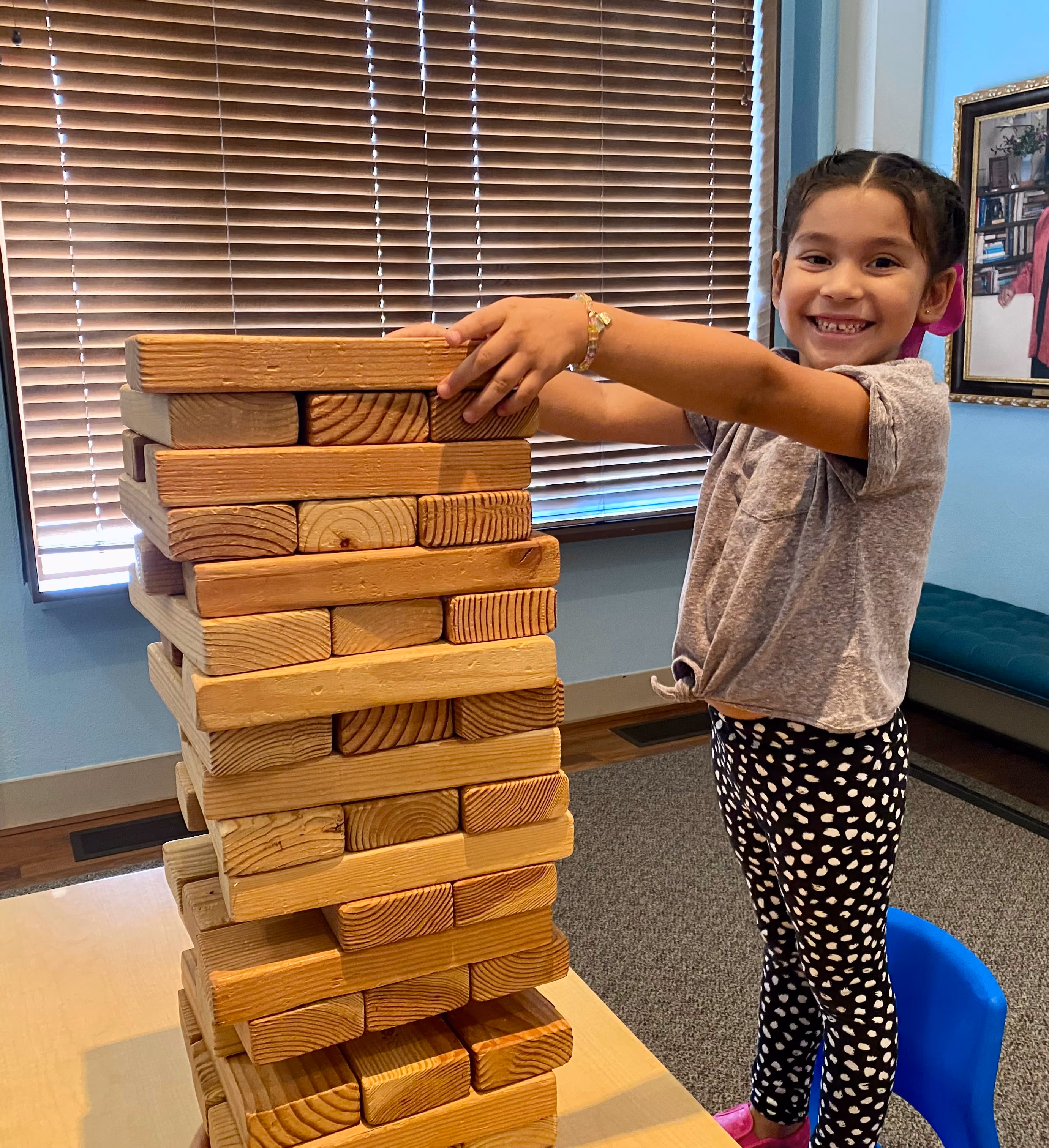 A young girl puts the final piece on top of a giant Jenga game.